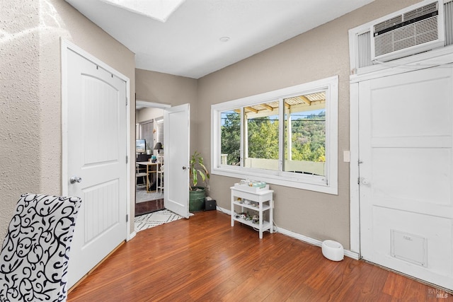 interior space with baseboards, a wall unit AC, and wood finished floors