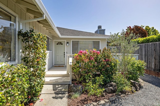 entrance to property with a shingled roof, fence, and a chimney