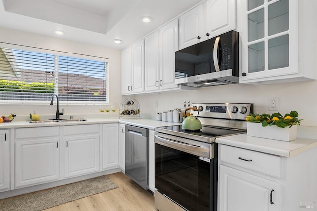 kitchen with glass insert cabinets, recessed lighting, a sink, light wood-style flooring, and appliances with stainless steel finishes