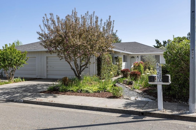 view of property hidden behind natural elements featuring a garage, concrete driveway, and roof with shingles