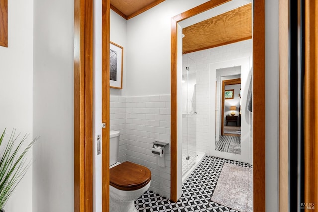 full bath featuring wainscoting, a stall shower, toilet, and tile walls