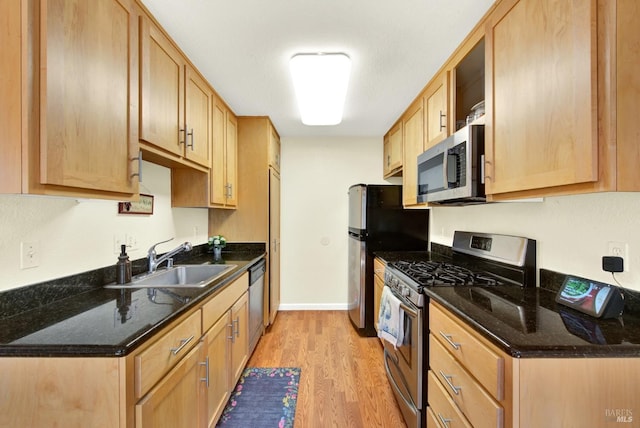 kitchen with a sink, light wood finished floors, dark stone counters, stainless steel appliances, and baseboards