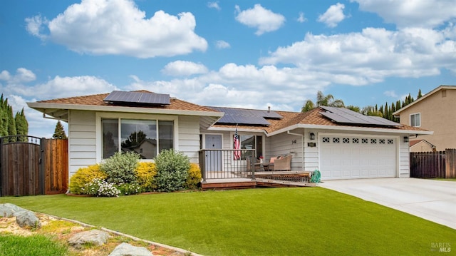 view of front facade featuring a front yard, driveway, roof mounted solar panels, an attached garage, and fence