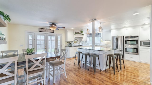 kitchen with appliances with stainless steel finishes, a breakfast bar area, light wood finished floors, and white cabinetry