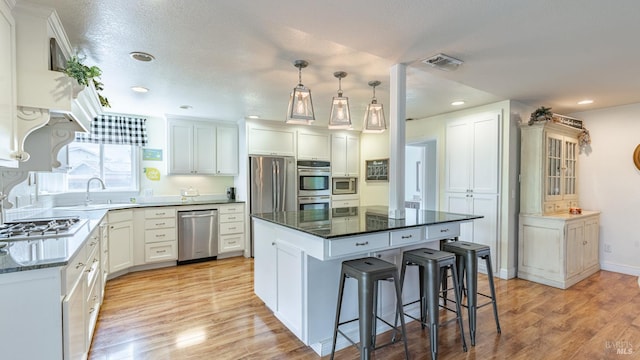 kitchen featuring stainless steel appliances, a kitchen breakfast bar, light wood-type flooring, a center island, and visible vents