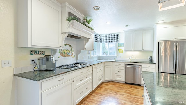 kitchen with dark stone counters, white cabinets, appliances with stainless steel finishes, and a sink