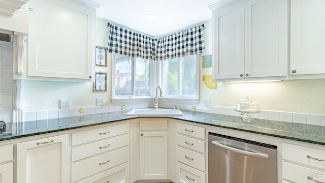 kitchen with dark stone countertops, white cabinetry, stainless steel dishwasher, and a sink