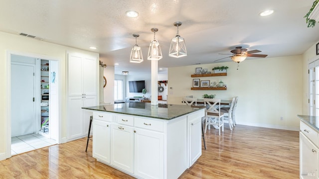 kitchen with light wood-style floors, ceiling fan, a center island, white cabinetry, and visible vents