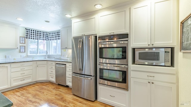 kitchen featuring a textured ceiling, white cabinets, a sink, appliances with stainless steel finishes, and light wood-type flooring