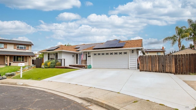 single story home featuring a front yard, a garage, driveway, solar panels, and fence