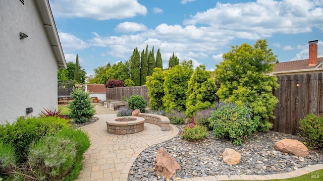 view of yard with a patio, an outdoor structure, a fenced backyard, a storage shed, and a fire pit