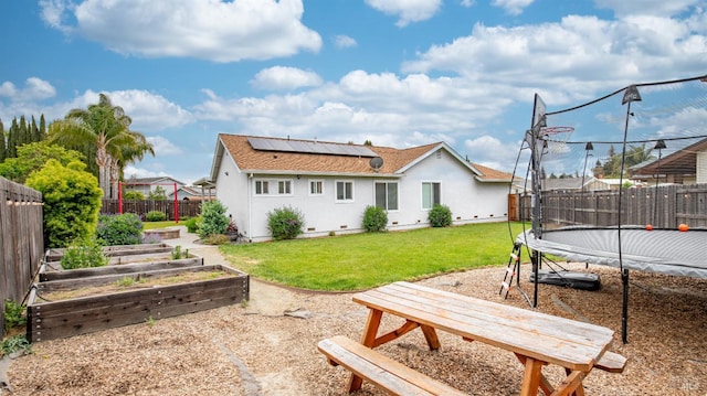 rear view of property with a trampoline, a fenced backyard, a lawn, a vegetable garden, and solar panels