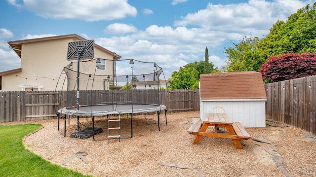 view of playground featuring an outbuilding, a trampoline, a storage unit, and a fenced backyard