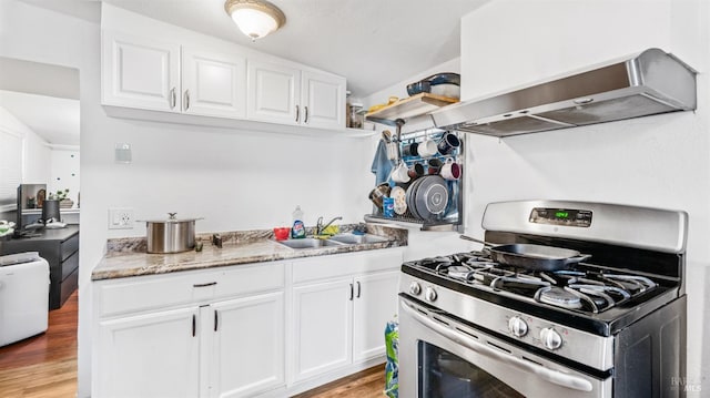 kitchen with white cabinets, gas range, wall chimney exhaust hood, and a sink