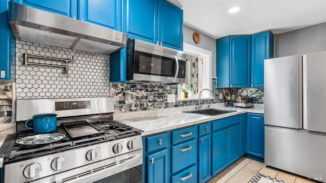 kitchen featuring tasteful backsplash, blue cabinetry, under cabinet range hood, appliances with stainless steel finishes, and a sink