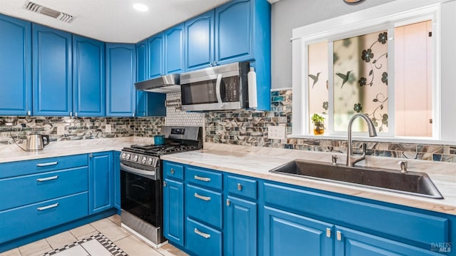 kitchen with blue cabinetry, appliances with stainless steel finishes, light countertops, backsplash, and a sink
