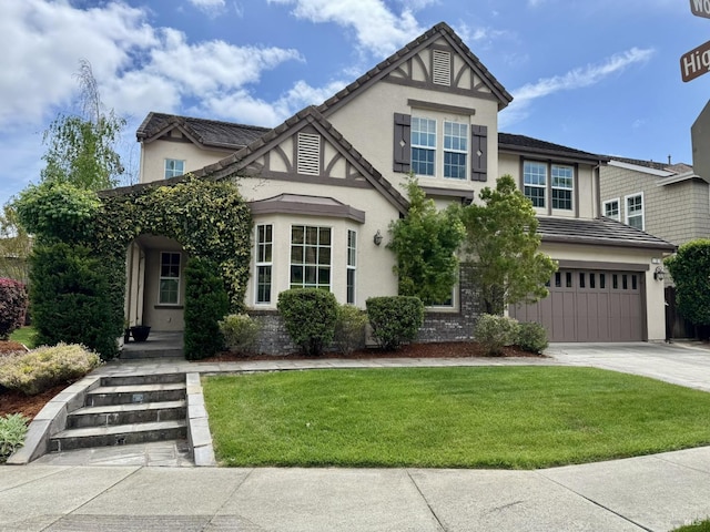 english style home featuring stucco siding, an attached garage, driveway, and a front lawn