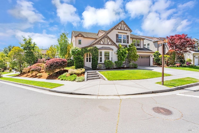 tudor-style house featuring an attached garage, stucco siding, concrete driveway, and a front lawn