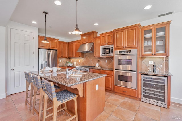 kitchen with brown cabinets, appliances with stainless steel finishes, wine cooler, under cabinet range hood, and visible vents