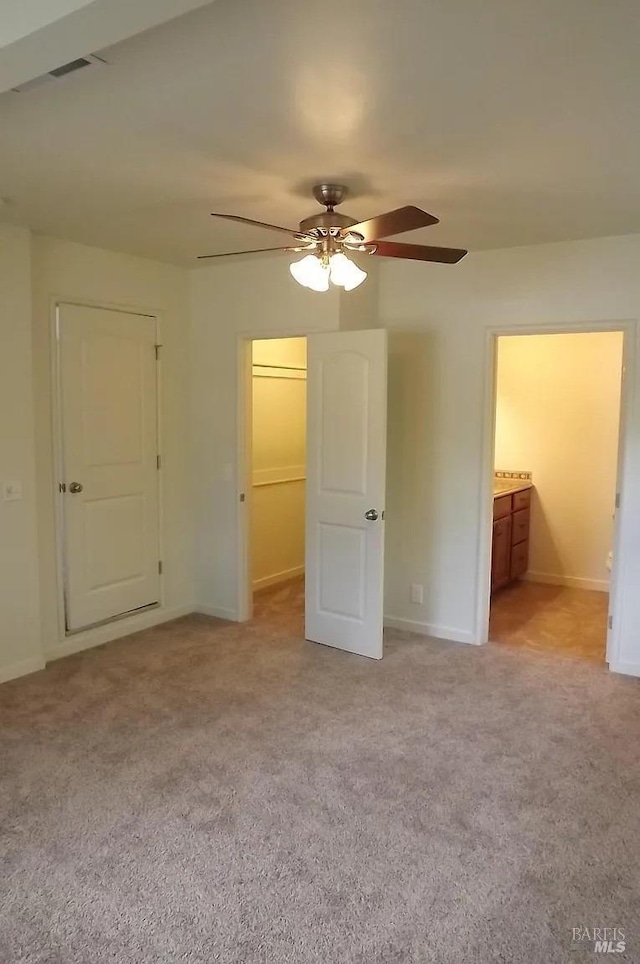 unfurnished bedroom featuring connected bathroom, a spacious closet, light carpet, and baseboards