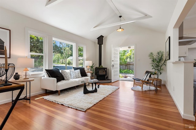 living area featuring light wood-type flooring, a wood stove, and lofted ceiling with beams