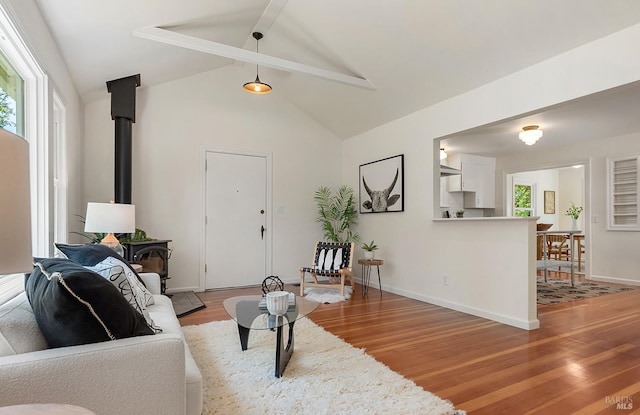 living room featuring vaulted ceiling with beams, a wood stove, light wood finished floors, and a wealth of natural light