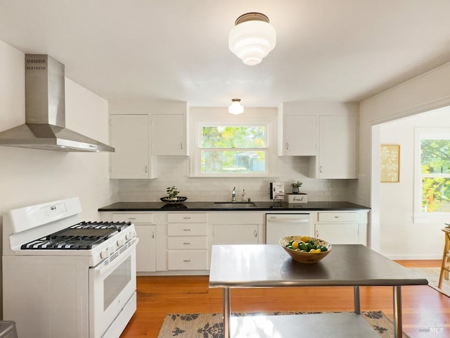 kitchen featuring wall chimney range hood, tasteful backsplash, a sink, white appliances, and white cabinetry