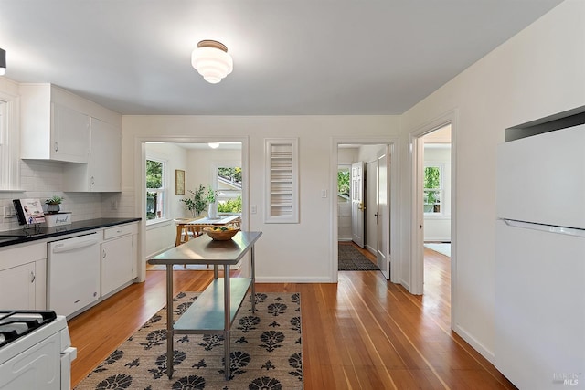 kitchen with dark countertops, light wood finished floors, backsplash, and white appliances