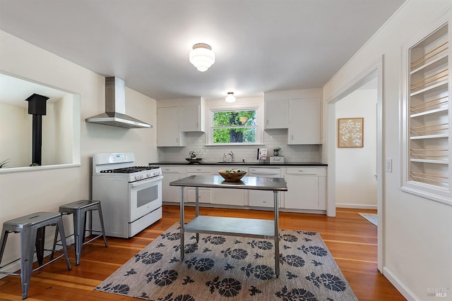 kitchen with white gas range oven, dark countertops, wall chimney exhaust hood, a sink, and backsplash