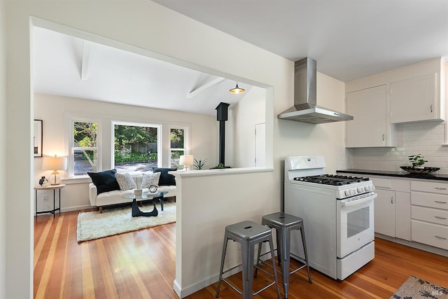 kitchen featuring decorative backsplash, white range with gas cooktop, wall chimney exhaust hood, and light wood-type flooring