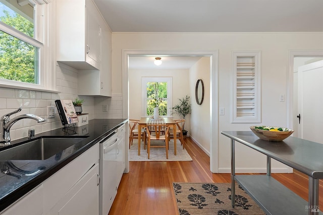 kitchen featuring white cabinets, a sink, dishwasher, light wood-style flooring, and decorative backsplash