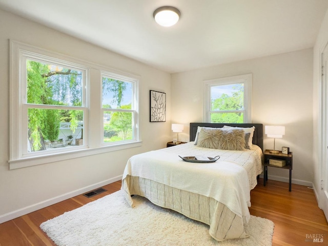 bedroom with baseboards, visible vents, multiple windows, and wood finished floors