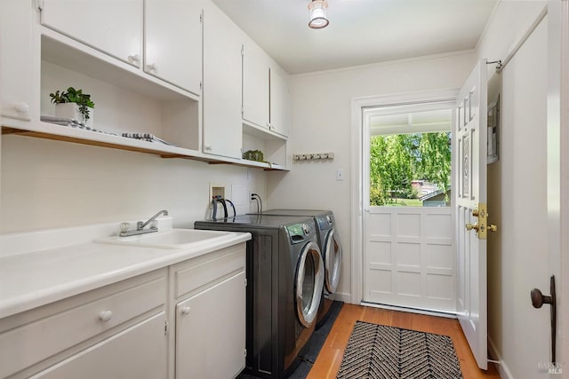 clothes washing area featuring a sink, light wood-style flooring, independent washer and dryer, and cabinet space