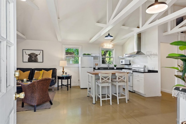kitchen featuring wall chimney range hood, beam ceiling, finished concrete flooring, white appliances, and white cabinetry