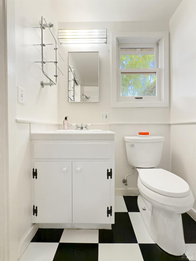 half bathroom featuring tile patterned floors, baseboards, vanity, and toilet