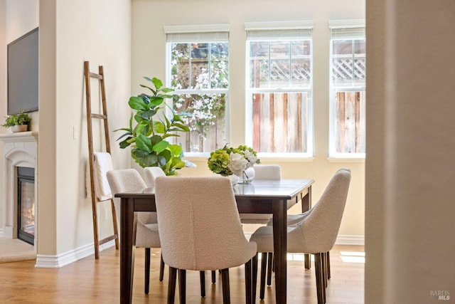 dining room featuring light wood finished floors, a glass covered fireplace, and baseboards