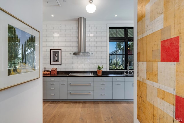 kitchen featuring cooktop, light wood-style flooring, wall chimney range hood, dark countertops, and gray cabinetry