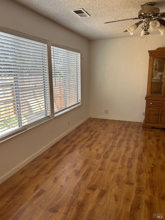 unfurnished room featuring a ceiling fan, visible vents, wood finished floors, and a healthy amount of sunlight