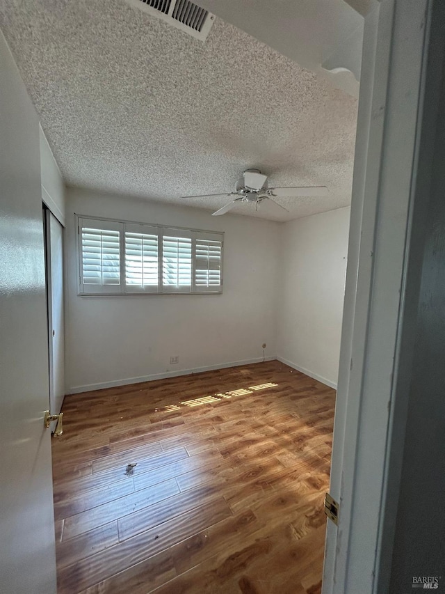 spare room featuring a textured ceiling, ceiling fan, wood finished floors, and visible vents