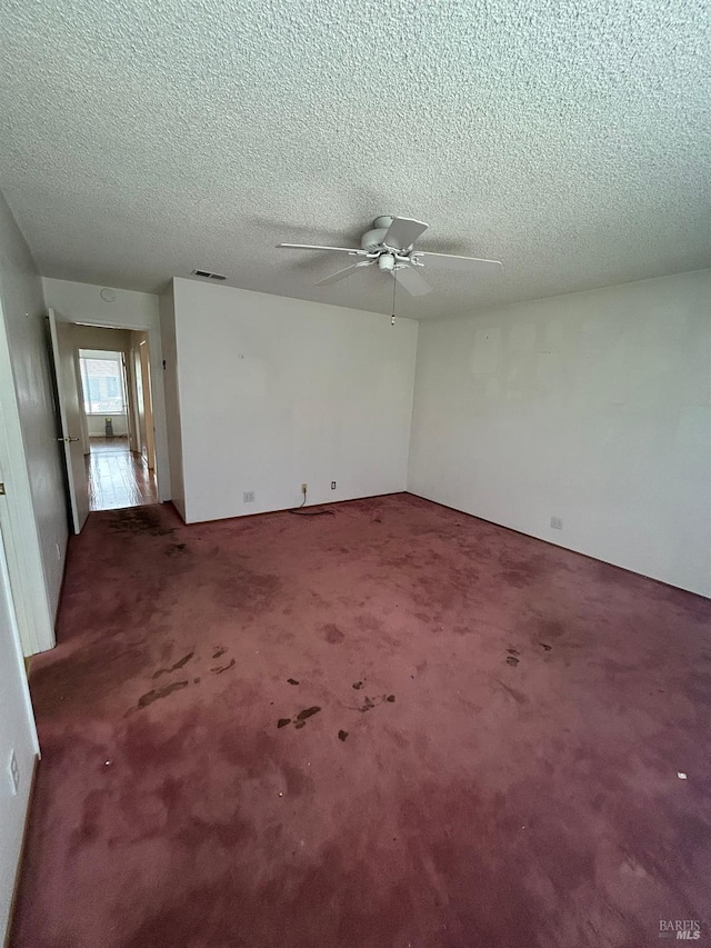 carpeted spare room with visible vents, ceiling fan, and a textured ceiling