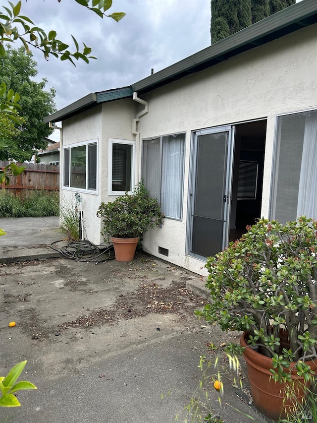 view of exterior entry with fence, crawl space, stucco siding, and a patio area