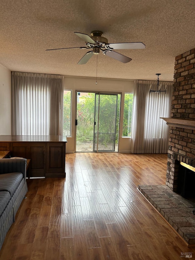 living room with a brick fireplace, a textured ceiling, a ceiling fan, and wood finished floors