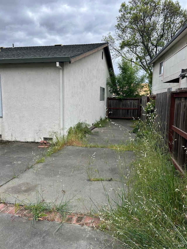 view of side of property featuring fence, a patio, stucco siding, and a shingled roof