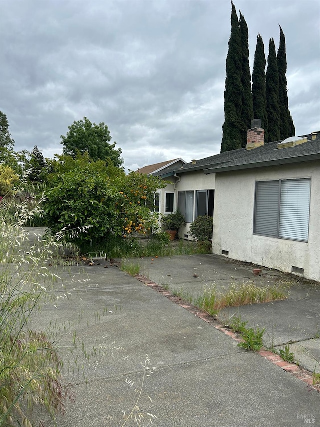view of side of home featuring a chimney, stucco siding, and roof with shingles