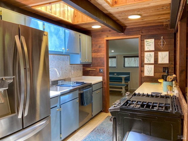 kitchen with light tile patterned floors, tasteful backsplash, appliances with stainless steel finishes, wood walls, and light countertops