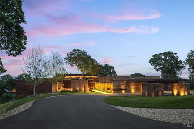 view of front of house featuring a lawn, stone siding, and curved driveway