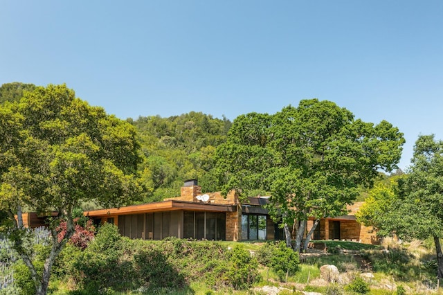 back of house with a chimney, board and batten siding, a forest view, and a sunroom