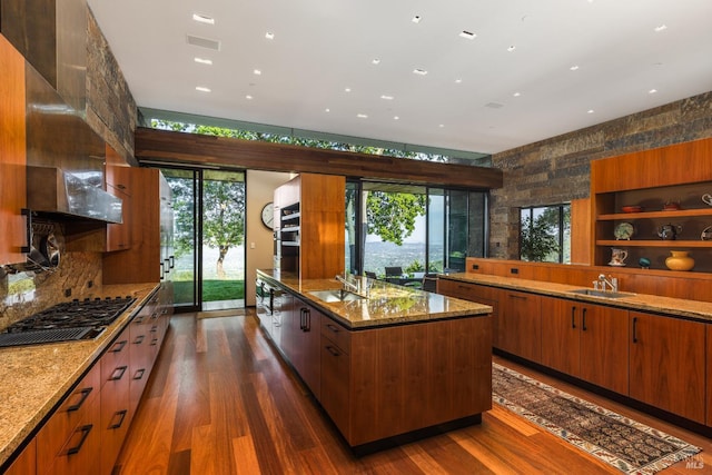 kitchen featuring light stone countertops, stainless steel gas cooktop, a healthy amount of sunlight, and a large island with sink