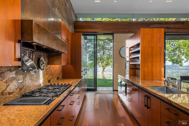 kitchen featuring a sink, tasteful backsplash, dark wood-type flooring, wall chimney range hood, and stone countertops