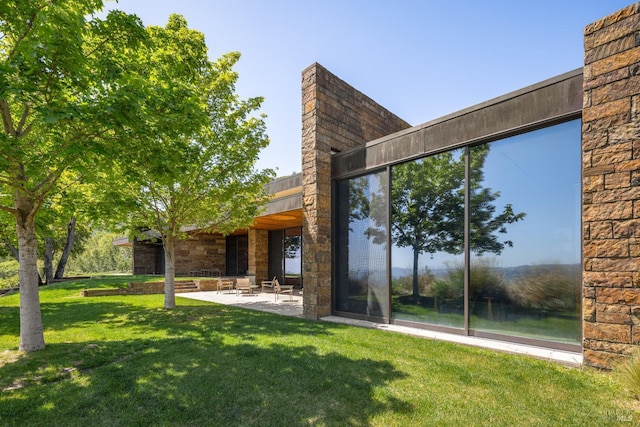back of property featuring a patio, stone siding, and a lawn